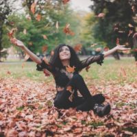 smiling woman in black top sitting on dried leaves