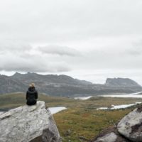 donna con giacca nera seduta su una roccia grigia