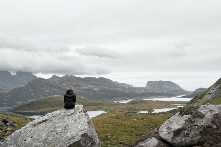 woman in black jacket sitting on gray rock