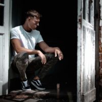 hombre con camiseta blanca sentado junto a puerta blanca