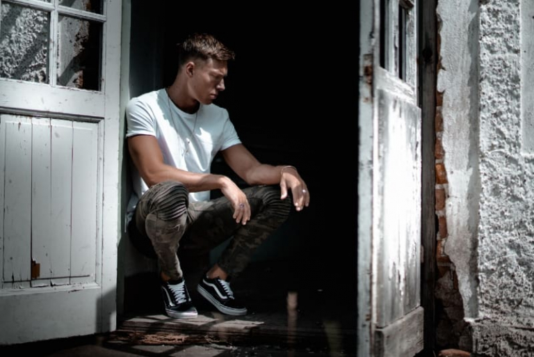 man in white t-shirt sitting beside white door