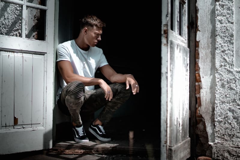 man in white t-shirt sitting beside white door