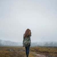 mulher de pé num campo aberto em direção a uma montanha nublada