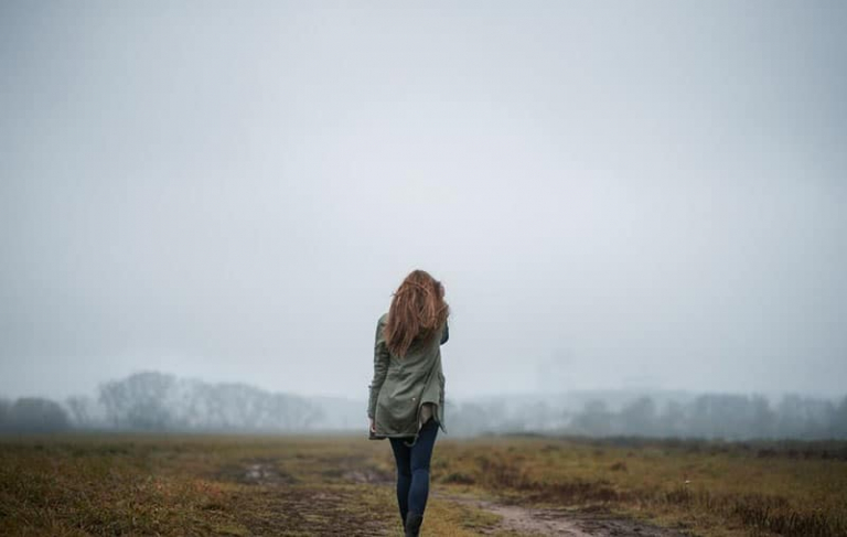 woman standing in an open field going to a clouded mountain