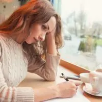 woman writing on a paper inside a cafe with a tea pitcher on the table