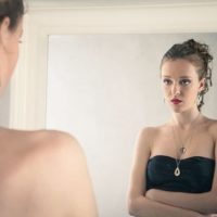 woman in black dress facing the mirror looking thoughtfully