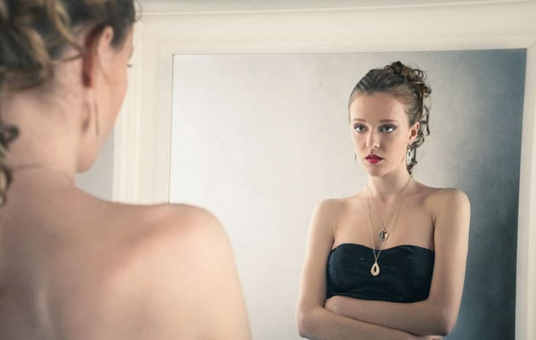 woman in black dress facing the mirror looking thoughtfully
