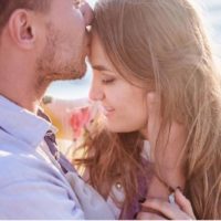 man kissing woman's forehead and hugging her outdoors