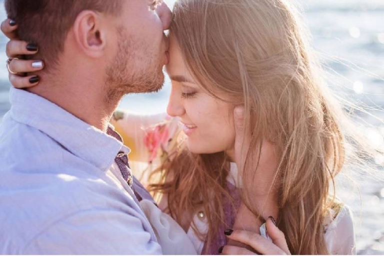 man kissing woman's forehead and hugging her outdoors