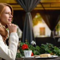 mujer desayunando en un café al aire libre con plantas y cortinas cerca de ella