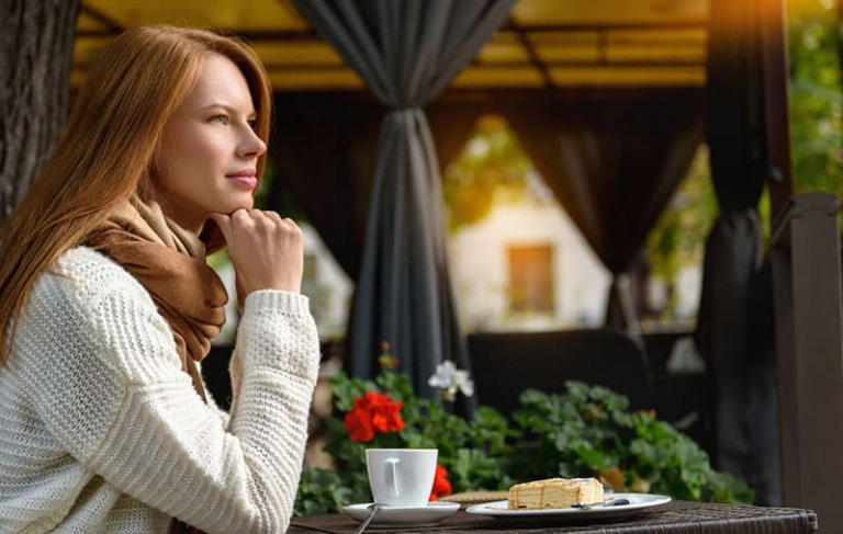 woman having breakfast at an outdoor cafe with plants and curtains near her