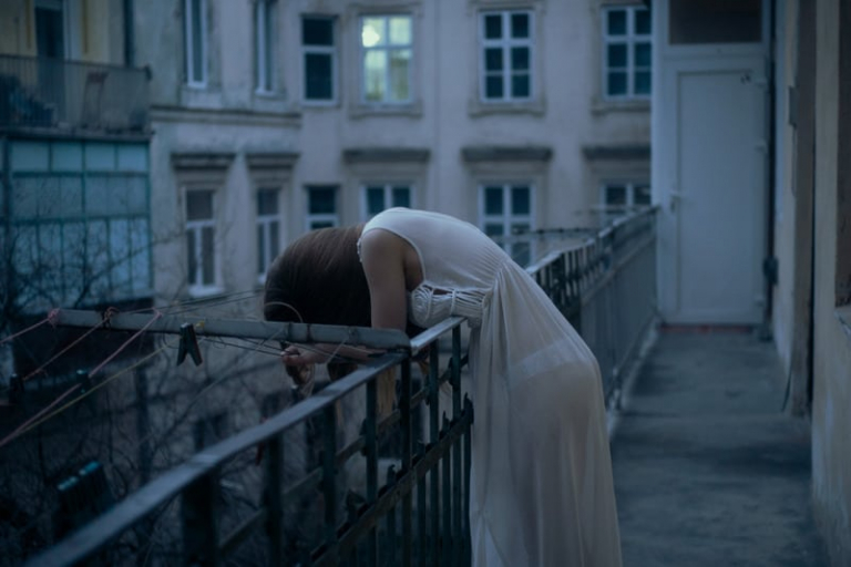 woman in night gown crying and leaning on the railings outside of a building during golden hour