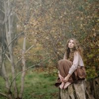 woman with curly hair sitting on wood log