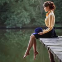 sideview of a woman sitting dreamy in the wooden platform of the lake barefooted