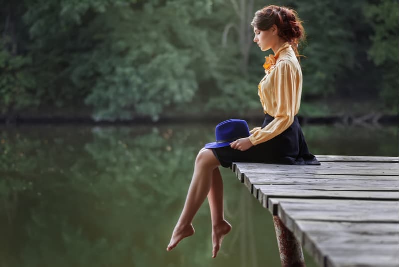 sideview of a woman sitting dreamy in the wooden platform of the lake barefooted