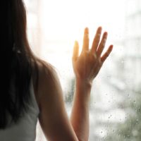 sad woman holding hand on the window glass