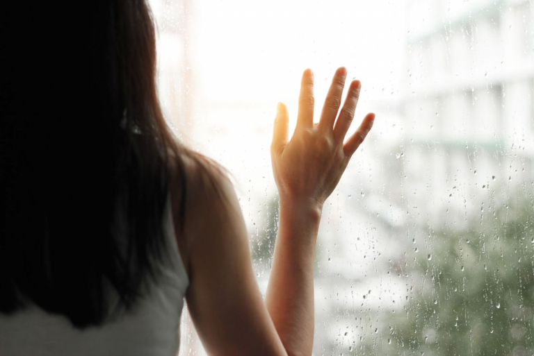 mujer triste con la mano en el cristal de la ventana