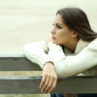 Mujer joven y solitaria sentada en un banco del parque