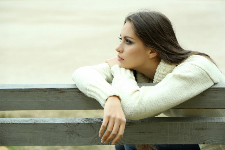 Young lonely woman sitting on bench in park