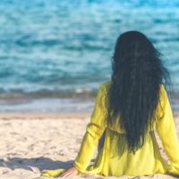 mujer con vestido amarillo sentada en la arena mirando al mar