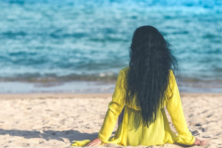 donna in abito giallo seduta sulla sabbia che guarda il mare