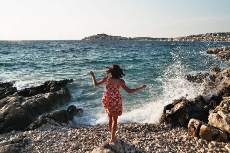 woman in dress standing on seashore near sea