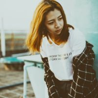 sad woman in white t-shirt standing near wall