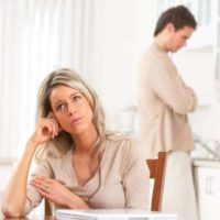 problematic couple with man standing and woman sitting by the table inside room