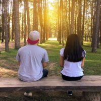 hombre con gorra y mujer sentados en un banco en el bosque