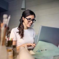 mulher com óculos a utilizar um computador portátil enquanto está sentada à mesa