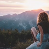 mujer sentada en una roca mirando la montaña