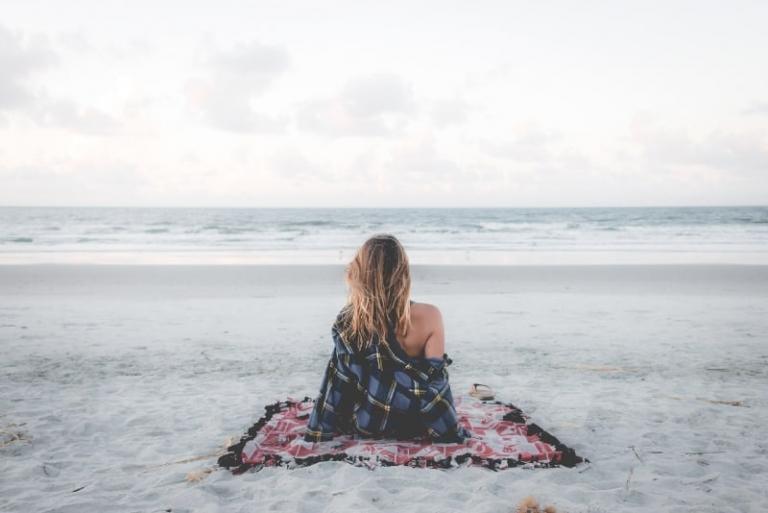 mujer sentada en una manta en la playa mirando al oceano