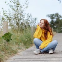 mulher a relaxar na natureza, sentada de pernas cruzadas num passeio de madeira