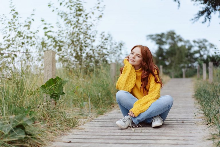 woman relaxing in nature sitting cross legged on a wooden boardwalk