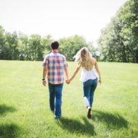 man and woman holding hands while walking through grass