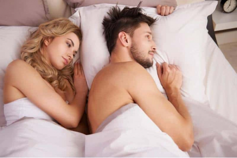 couple thinking while lying on bed with white linen