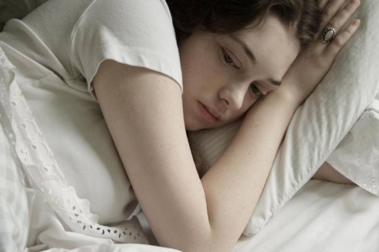sad woman lying down in bed facing the left side of the bed
