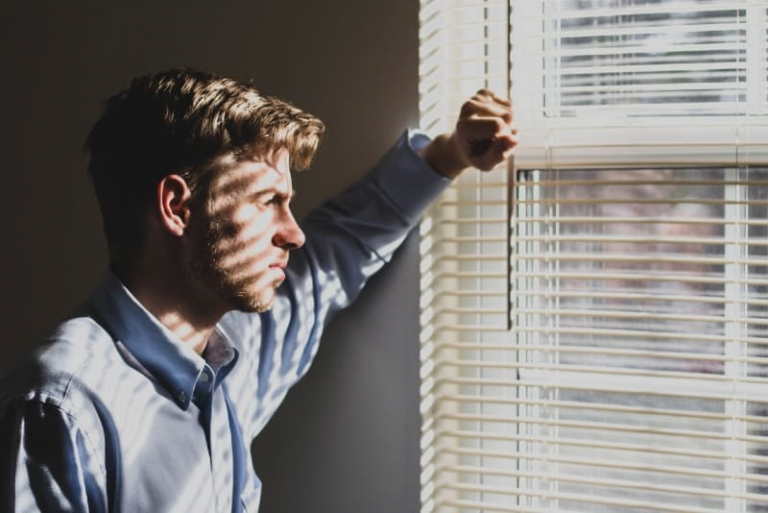 man in blue shirt standing near window blinds