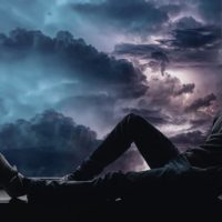 man sitting on the window sill looking outside thru a stormy weather