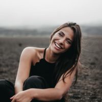 woman in black top smiling while sitting on ground