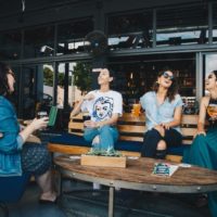 four women holding glasses of beer while sitting on bench