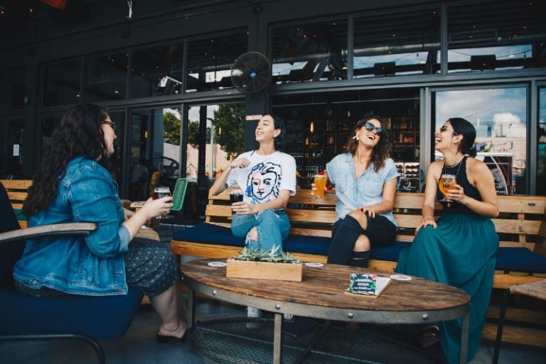 four women holding glasses of beer while sitting on bench
