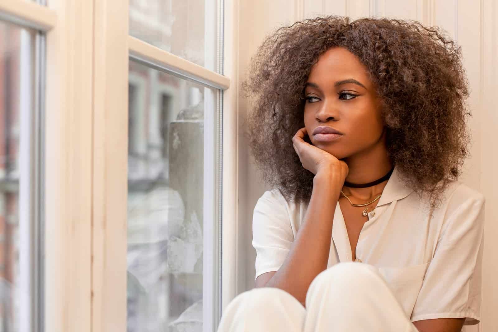 una triste mujer afroamericana sentada junto a la ventana