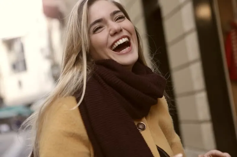 a woman laughing wearing brown trench coat 