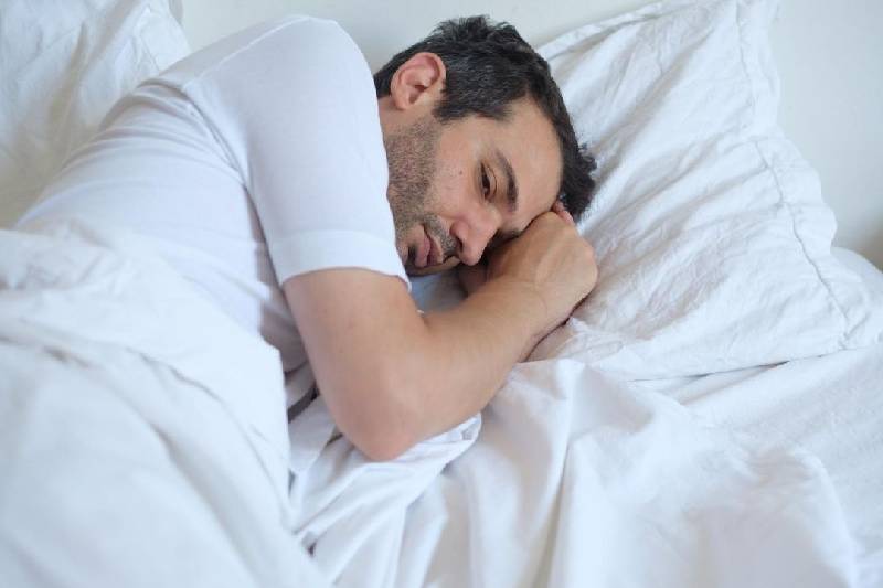 homem ansioso na cama deitado com cama de linho branco