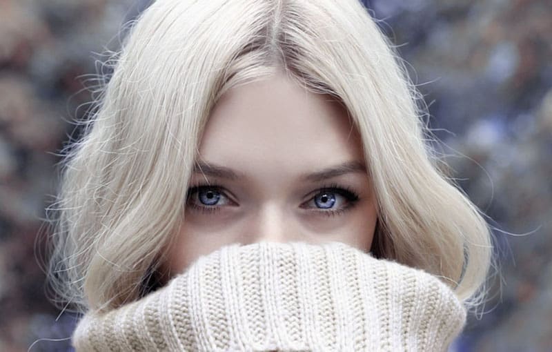 blue eyed woman's face in focus covering mouth with sweaters 