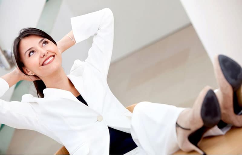 business woman sitting on desk hands on head and smiling