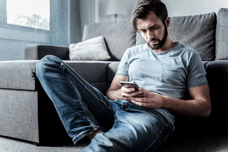 cheerles sad man looking at his cellphone and sitting on the floor near the sofa