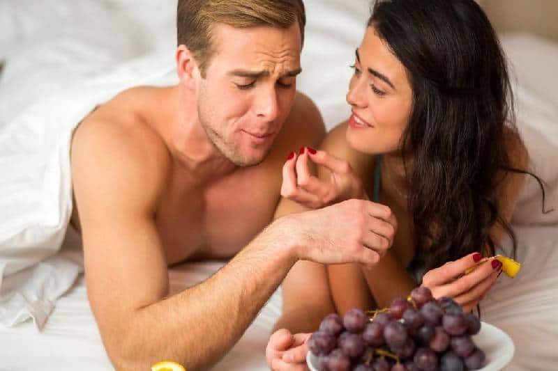 pareja comiendo frutas en la cama tapandose con manta