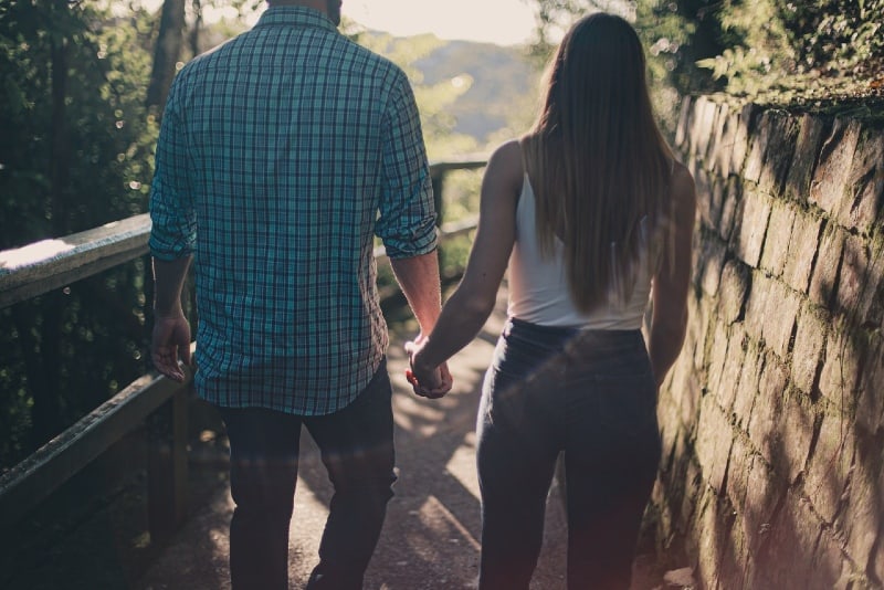 man and woman holding hands while walking along pathway